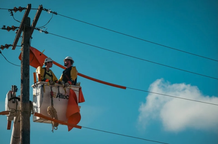 Two utility workers in a bucket truck, wearing hard hats, servicing power lines under a clear sky in Ocean County, New Jersey.
