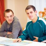A caregiver helping an adult with autism in a bright community day program, warm and natural lighting, candid style. In association with the Ocean County Career Center.